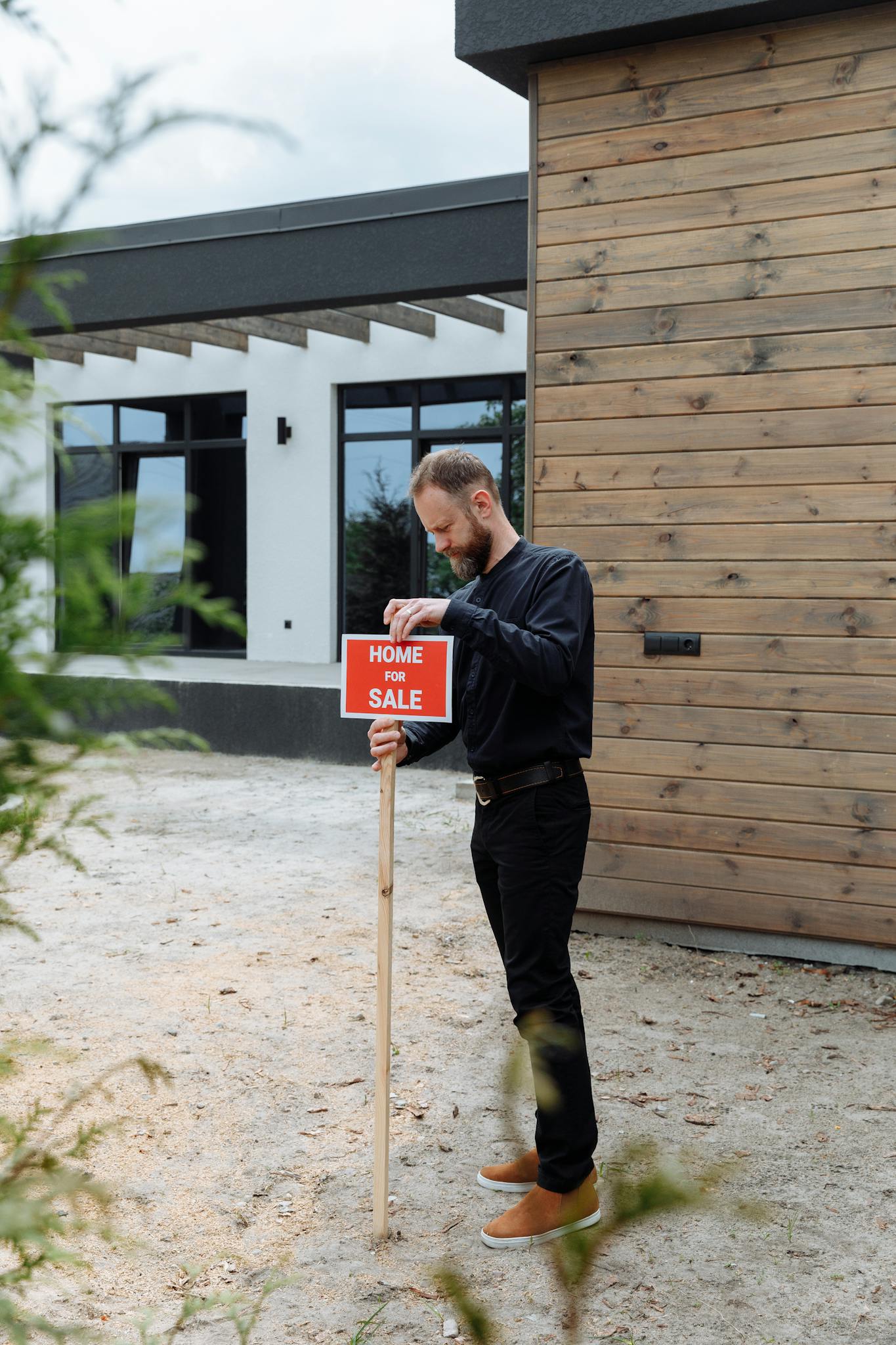A real estate agent holding a home for sale sign in front of a modern house.
